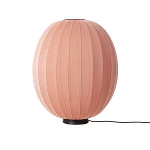 Oval gulvlampe i koral med strikket overflade, placeret på sort fod med ledning.